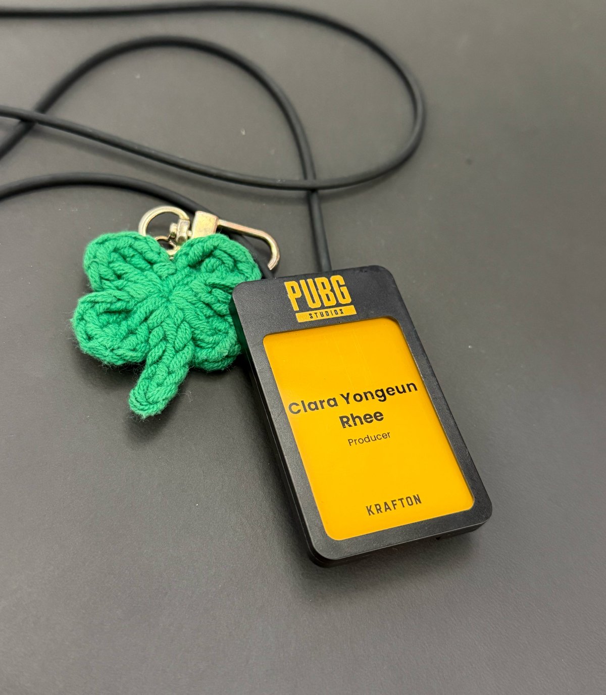 A PUBG Studios employee badge reading Clara Yongeun Rhee, Producer, Krafton, on a lanyard with a green crochet clover charm.